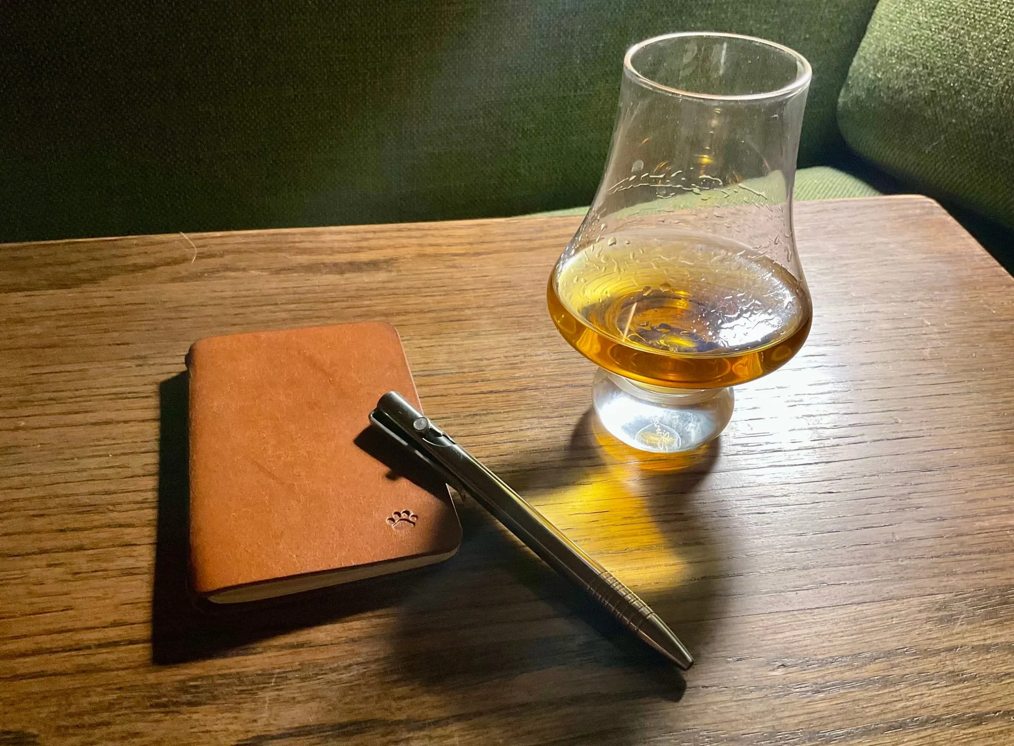 Writing desk with pen, pocket notebook, and a whiskey glass
